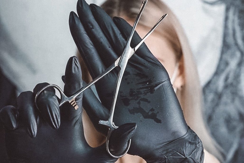 Piercer w rękawiczkach trzyma narzędzie do piercingu