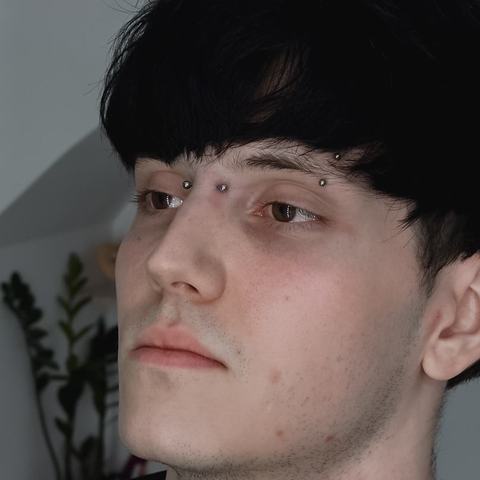 Piercing brwi subtelnie podkreśla profil. Srebrna biżuteria nadaje całości nowoczesny akcent.