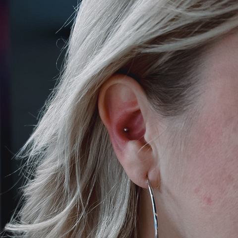 Piercing ucha podkreśla jego delikatny kształt. Podłużna biżuteria nadaje stylizacji lekki charakter.