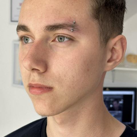 Piercing brwi subtelnie podkreśla spojrzenie. Drobna biżuteria nadaje całości nowoczesny charakter.