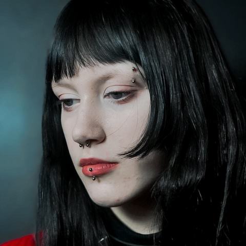 Vertical labret podkreśla dolną wargę. Czerwona biżuteria dodaje stylizacji wyrazistego akcentu.