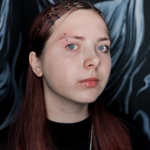 Piercing brwi przyciąga uwagę kolorowym akcentem. Delikatna biżuteria podkreśla spojrzenie.