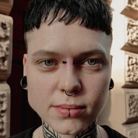 Septum i piercing dolnej wargi tworzą mocny akcent. Srebrna biżuteria podkreśla wyrazisty styl.