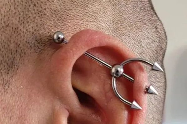 Srebrny piercing industrial w chrząstce ucha.