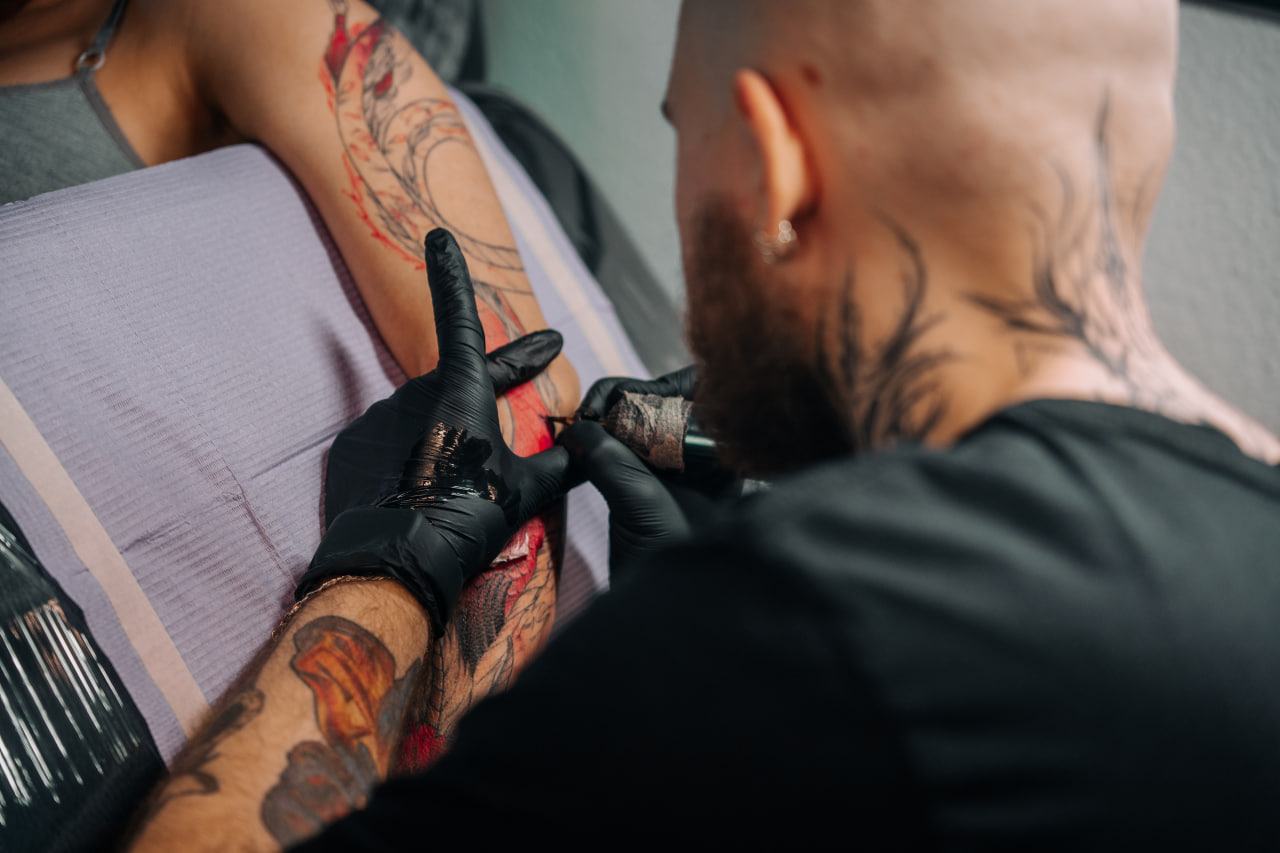 Tatuażysta w rękawiczkach tatuuje ramię klienta