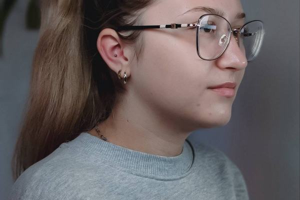 Piercing ucha z delikatną biżuterią u kobiety w okularach